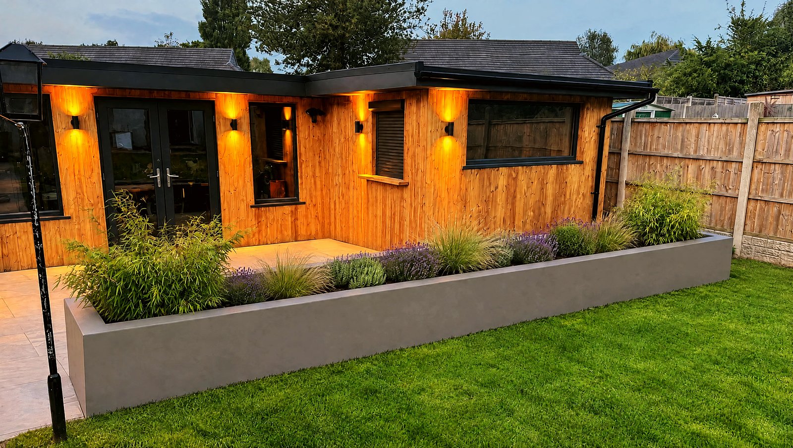 A long timber garden room at dusk with the wall lights on
